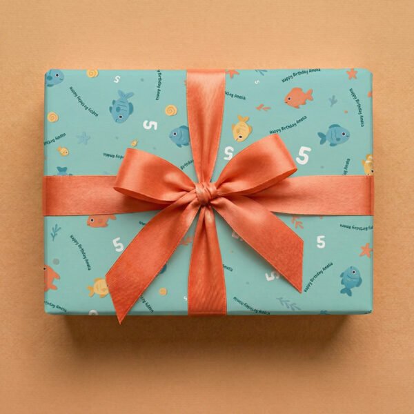 Turquoise wrapping paper with underwater-themed pattern wrapped as a gift box with a coral-red satin ribbon bow, featuring cartoon fish in various sizes and colors, spiral shells, starfish, seaweed, age number "5", and personalized "Happy Birthday Amelia" text on a neutral background.